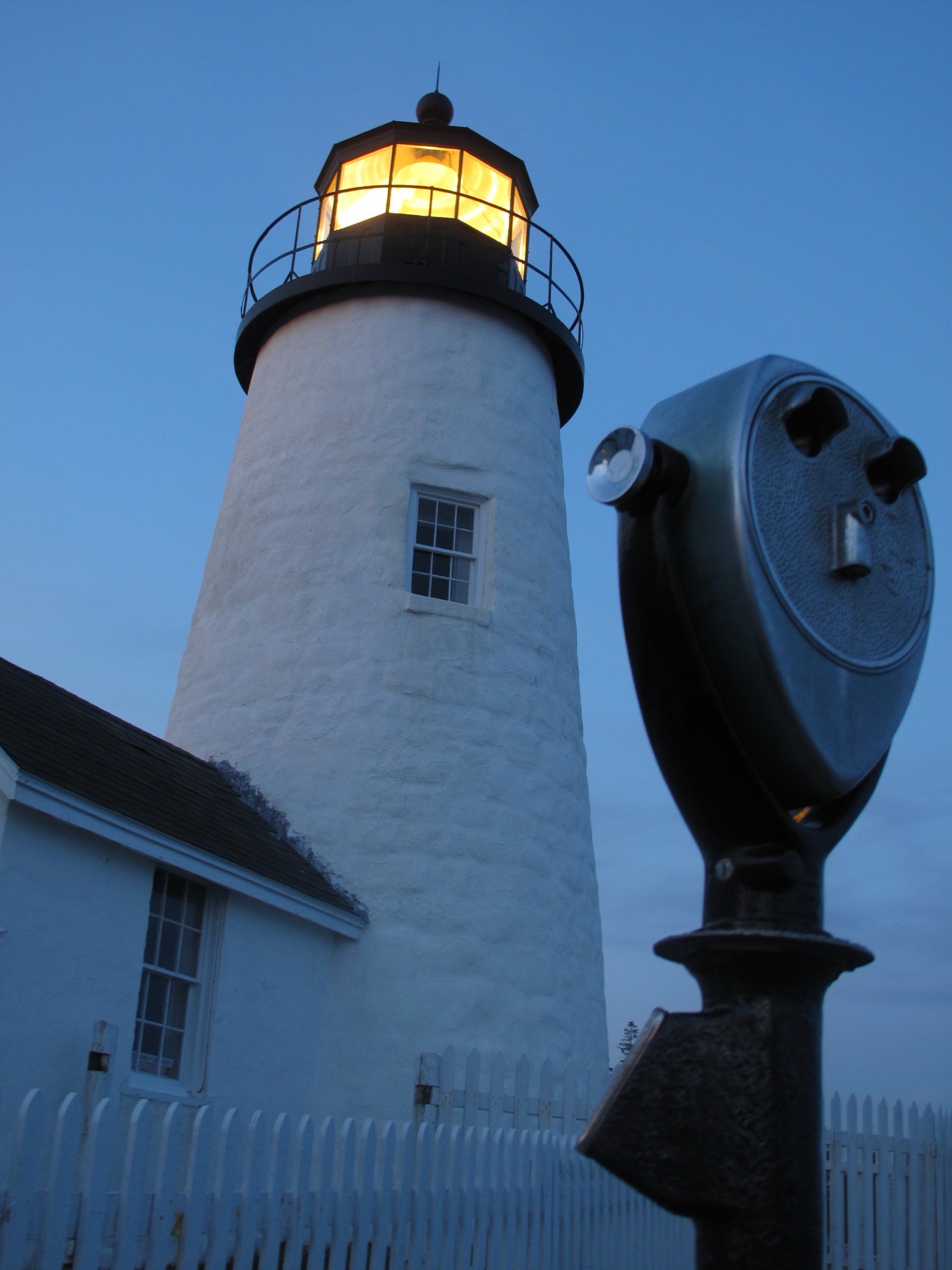 A Tower Optical viewer at dawn beside the lit Pemaquid Point lighthouse, Maine